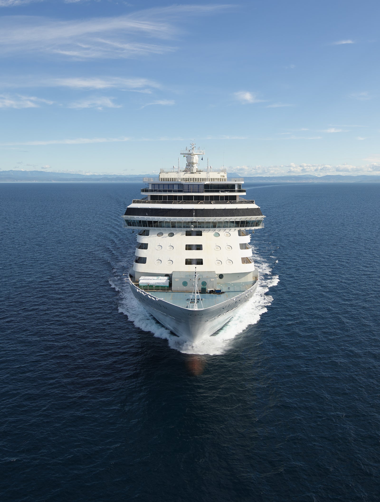 Fincantieri | Group - Business - Products - Cruise Ships - Seven Seas Splendor: Front view of large modern operational white cruise ship with multiple decks and visible lifeboats, sailing on calm open waters under clear and serene sky, tranquil atmosphere and sense of adventure.