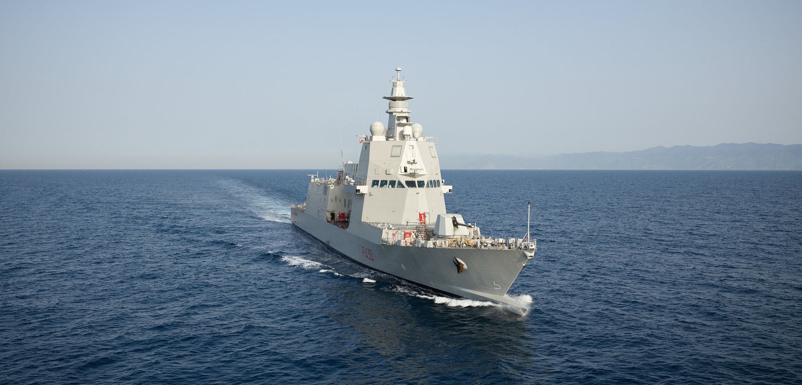  Fincantieri | Gruppo - Business - Prodotti - Navi per la difesa - Fregate - Classe Thaon de Revel: Vista laterale della nave operativa in navigazione, scafo grigio moderno, radar e antenne visibili, sfondo con sagome terrestri.