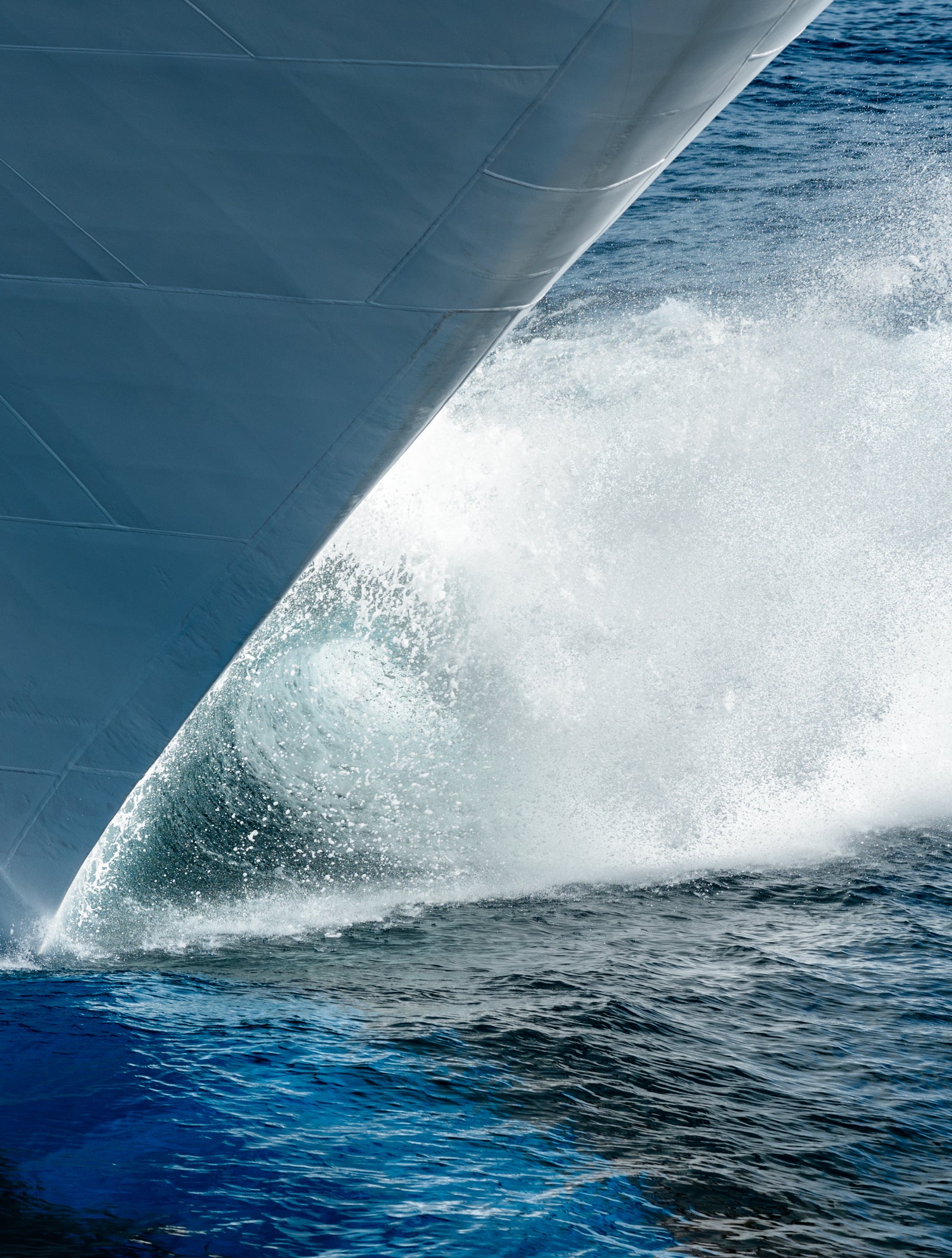 Fincantieri | Group - Business - Products - Cruise Ships - Carnival Horizon: Ship’s bow slicing through ocean, dynamic splashes and ripples, deep blue water contrasts with white spray, sharp angles emphasize sleek design and movement.