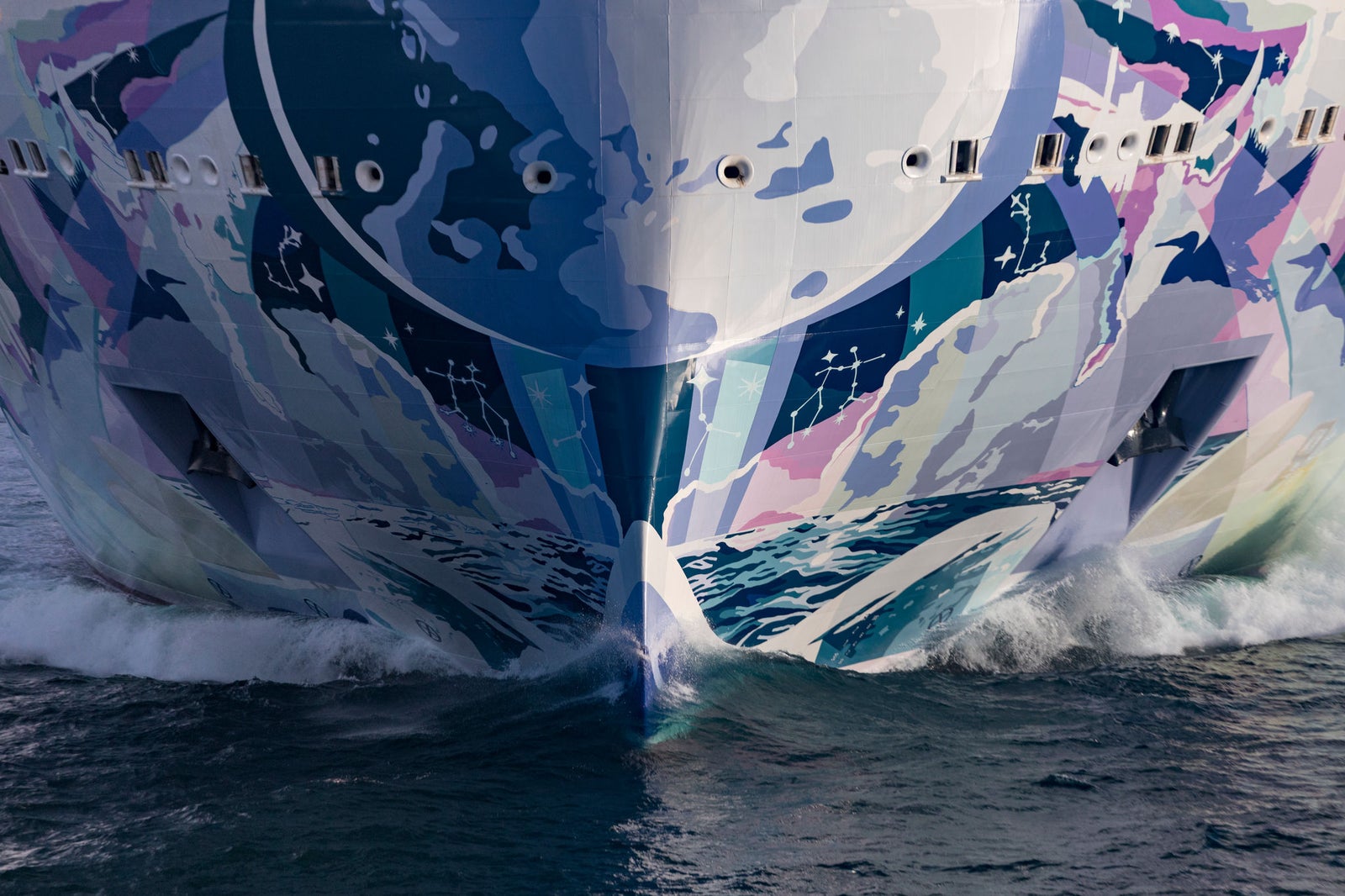 Fincantieri | Gruppo - Business - Prodotti - Navi da Crociera - Norwegian Luna: Vista della vibrante prua di grande nave operativa con scafo a strisce gialle, rosse e arancioni, movimento dinamico attraverso le onde in mare aperto.