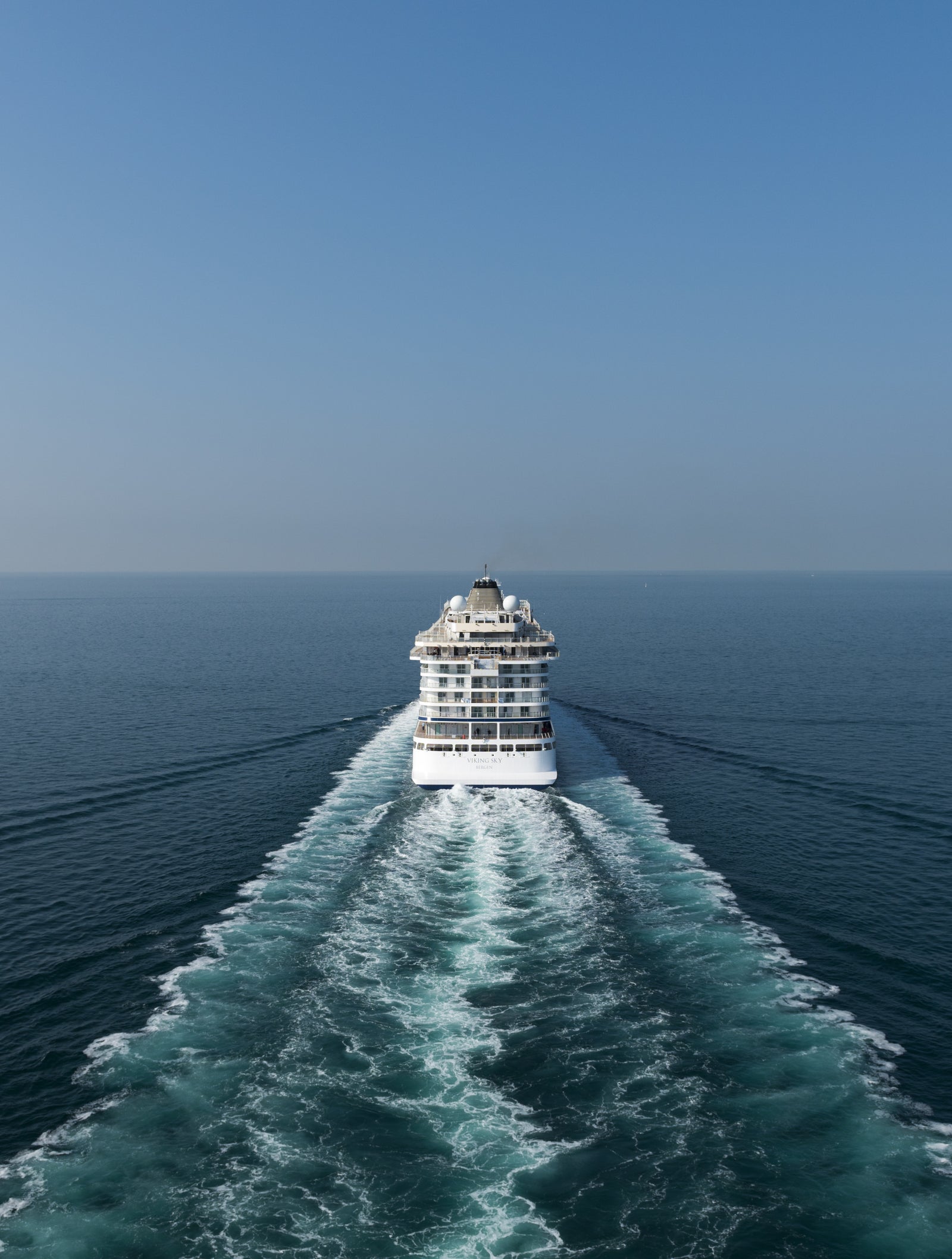 Fincantieri | Group - Business - Products - Cruise Ships - Viking Sky: Rear view of Viking Sky cruise ship in operation navigating open sea, visible white wake, "Viking Sky" name and registration port "Bergen" readable on stern, multi-deck structure with large windows and balconies.