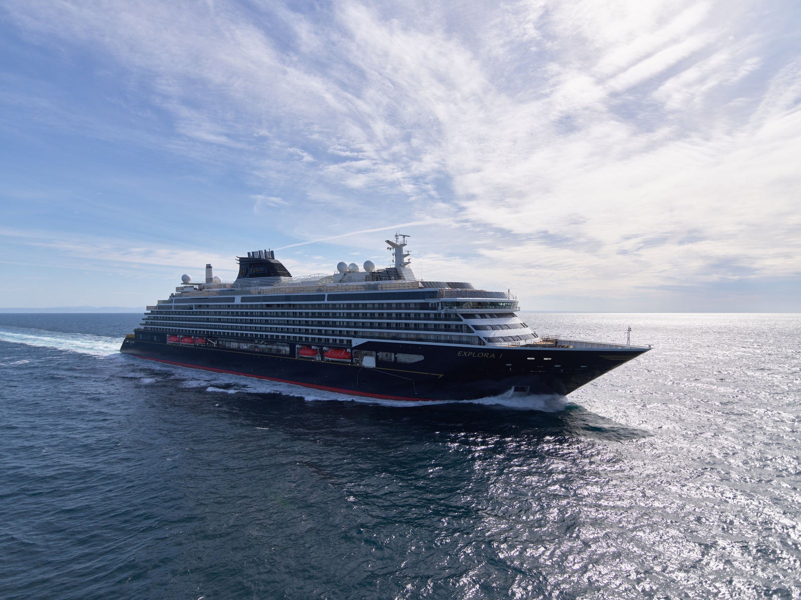 Fincantieri | Group - Business - Products - Cruise Ships - Explora I: Large luxury cruise ship in operation, gliding through calm ocean waters, sleek black and white design with visible red accents, partly cloudy sky, open sea, bright daylight.